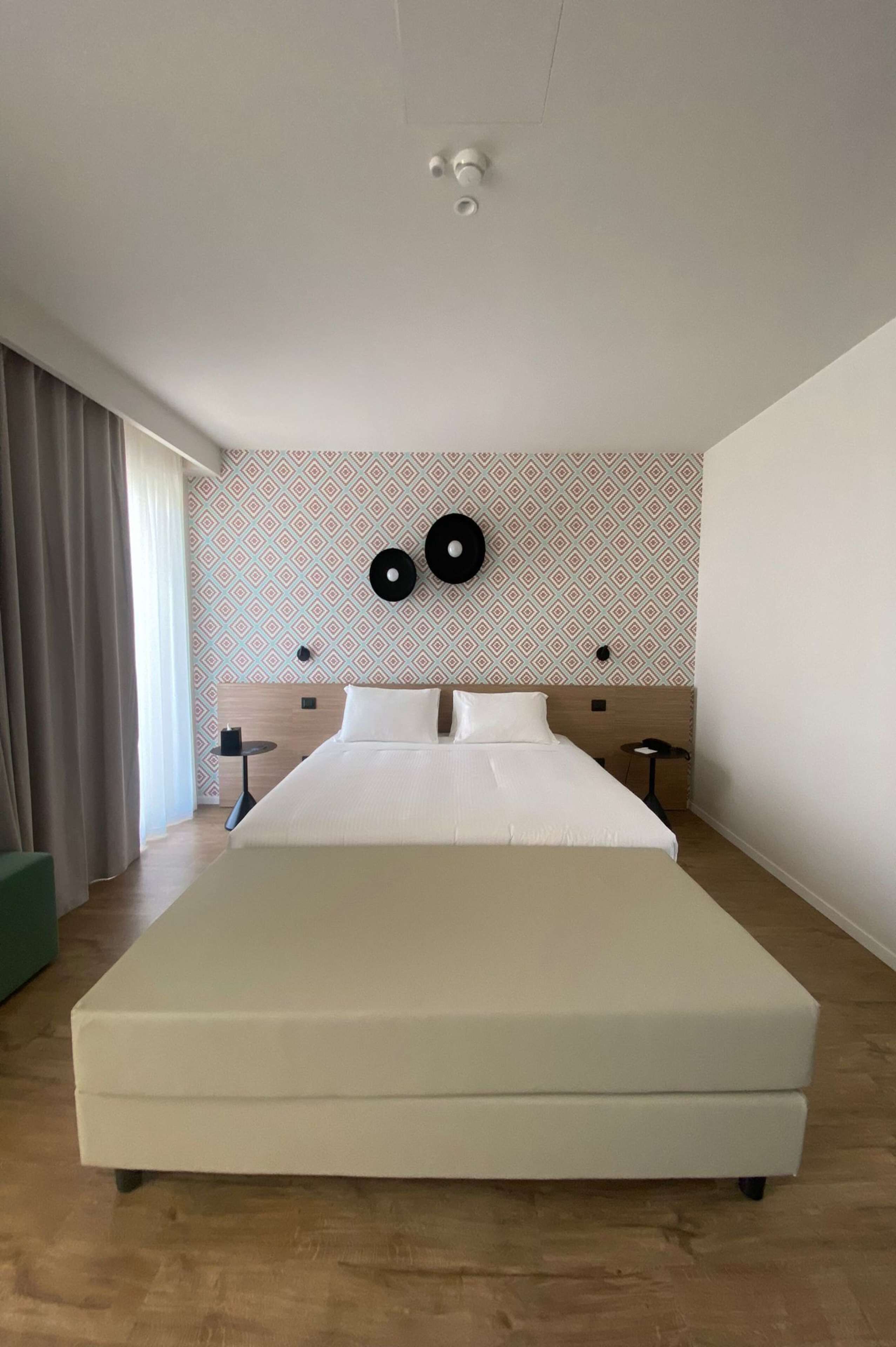 En stor seng på et hotelværelse med tapetvæg, et lille bord og et vindue med gardiner.