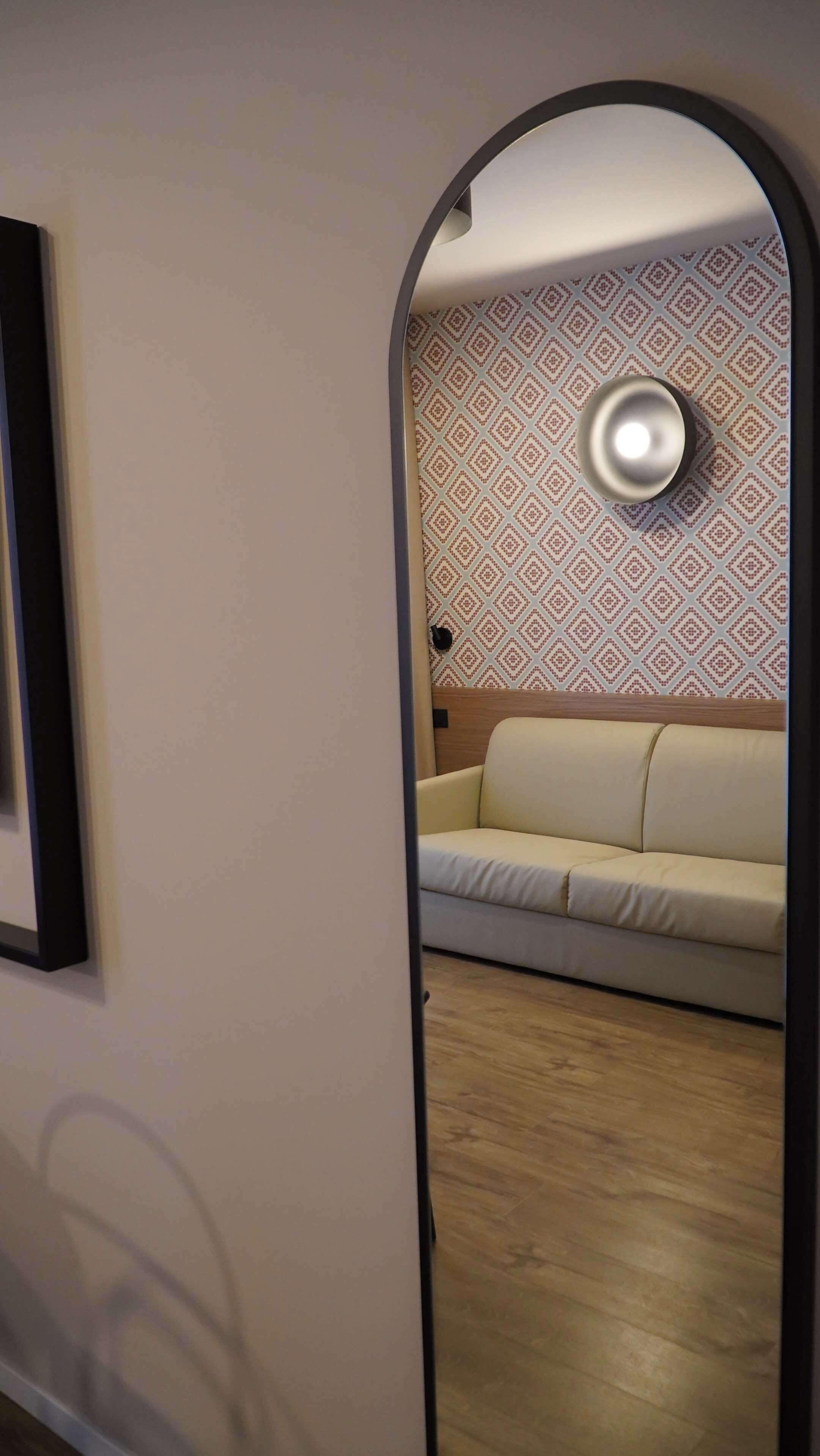 Un pasillo con un espejo que refleja una pared con diseño y un sofá color beige.