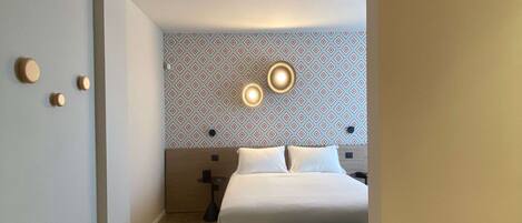 Una habitación de hotel con cama, mesitas de noche y un papel tapiz estampado.