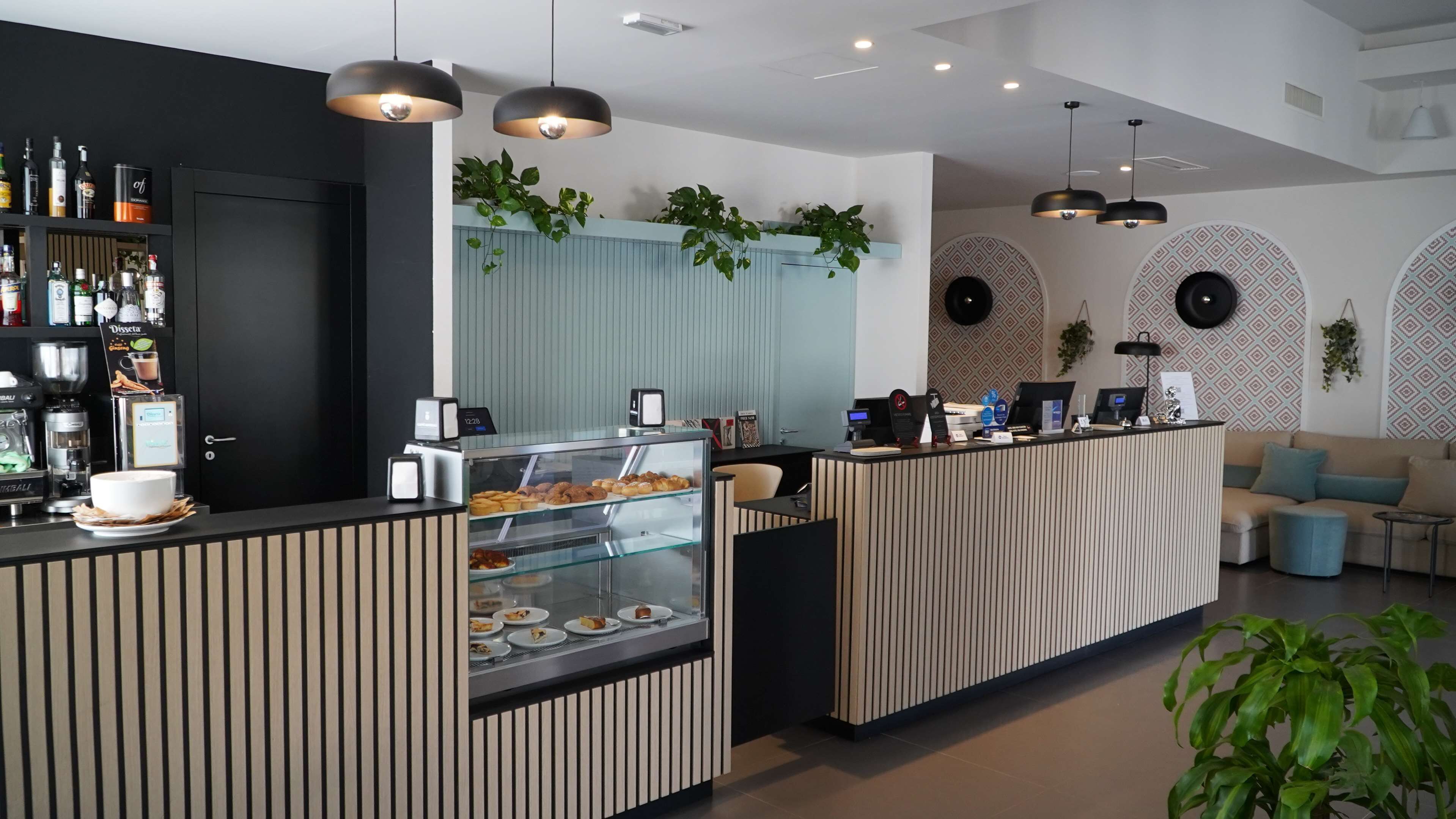 A modern bar area with a coffee machine, a glass display case with pastries, and a seating area with a sofa and chairs.