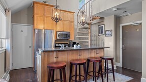 A kitchen with wooden cabinets, stainless steel appliances, a central island with stools, and a staircase. - Blue Mesa Lodge 40B by Avantstay Ski In/ Ski Out Unit w/ Balcony! (Telluride)