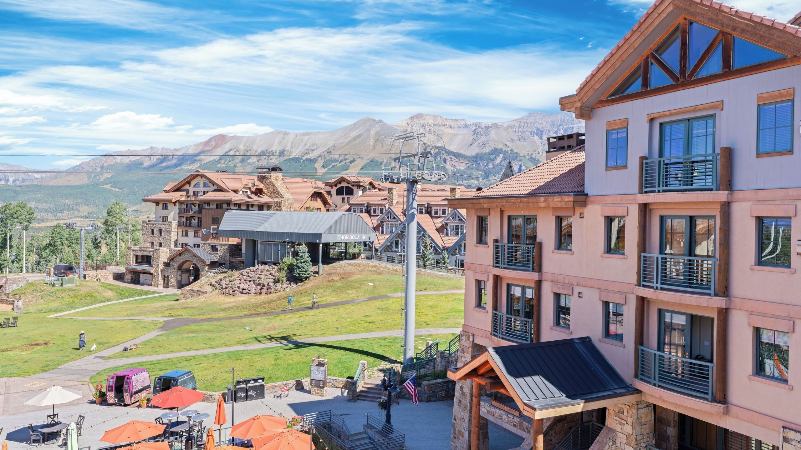 Un hotel con vista a la montaña, asientos al aire libre y un telesilla al fondo.