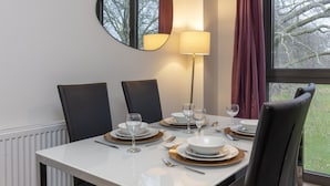 Mesa de comedor para cuatro con diseño moderno, un espejo redondo en la pared y vista a árboles por la ventana.