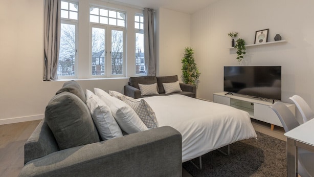 Un dormitorio moderno con una cama grande, un sofá gris y un televisor sobre un mueble.