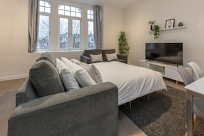 Een moderne slaapkamer met een groot bed, een grijze bank en een televisie op een dressoir.