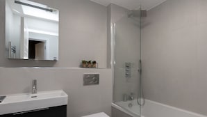 Un baño moderno con ducha envuelta en vidrio, un lavamanos blanco y un inodoro.