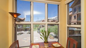 Uma sala de jantar com uma mesa, cadeiras, um abajur e vista para uma paisagem montanhosa através de amplas janelas.