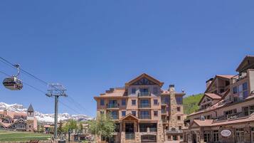 A multi-story hotel with a stone facade, a ski lift in the background, and a clear blue sky.