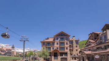 A multi-story hotel with a prominent entrance, a ski lift in the background, and a mountainous backdrop.