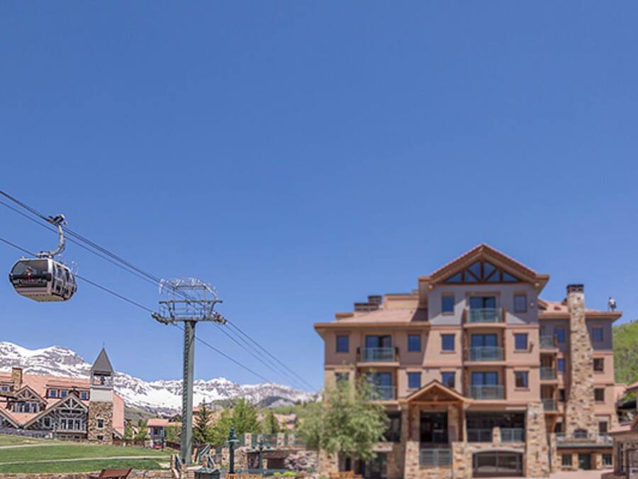 A multi-story hotel with a prominent entrance, a ski lift in the background, and a mountainous backdrop.