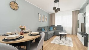 Un salon moderne avec un coin repas, un canapé gris et un téléviseur.