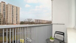 Un balcon avec une balustrade blanche, une petite table ronde sur laquelle est posée une plante en pot, et deux chaises noires.
