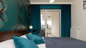 Ein modernes Hotelzimmer mit einem großen Bett, türkisgrünen Vorhängen und Blick auf die Stadt durch die Tür.