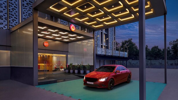 Un bâtiment moderne avec une voiture rouge garée devant, une enseigne avec un « C » rouge, et un plafond au design géométrique.