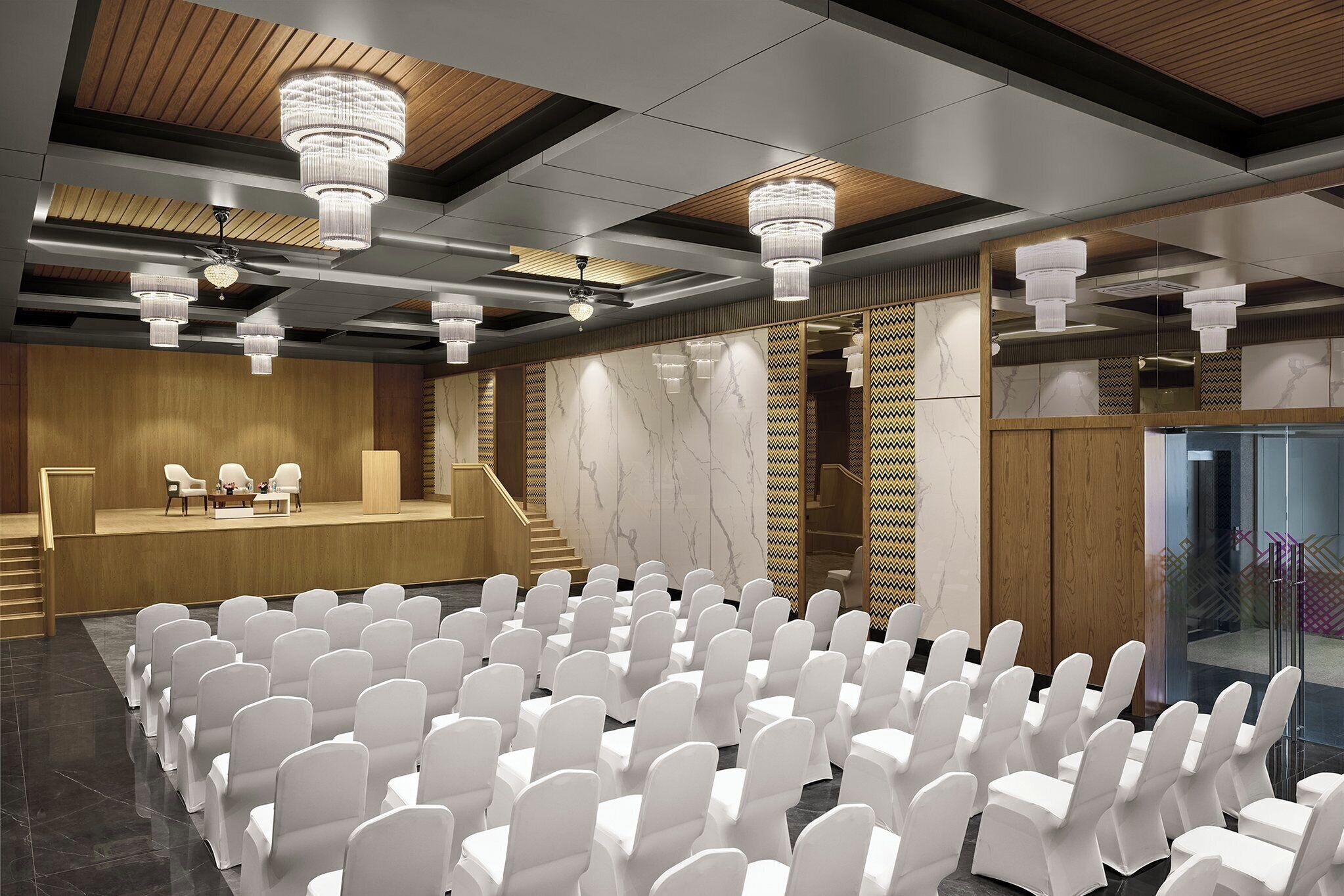 A conference room with rows of white chairs, a stage with two chairs, and a wooden panel wall.