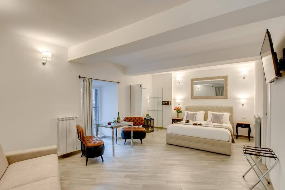 Quarto de hotel moderno com uma cama grande, área de estar com mesa e cadeiras, radiador e vista para o exterior.