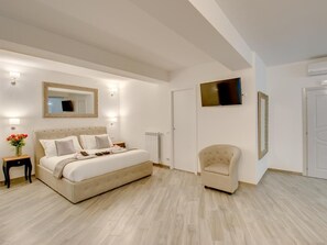 A bedroom with a large bed, a bedside table with a vase of flowers, a chair, a TV mounted on the wall, and a door. - Roma Suites Navona (Rome)