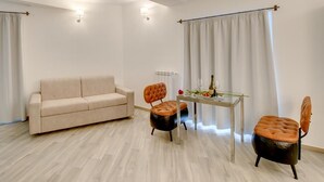 A modern living room with a beige sofa, two leather armchairs, a glass coffee table, and a dining table with a bottle and glasses. - Roma Suites Navona (Rome)