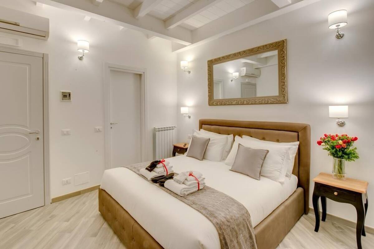 Quarto bem arrumado com uma cama grande, mesas de cabeceira, um espelho e um candeeiro fixado na parede.