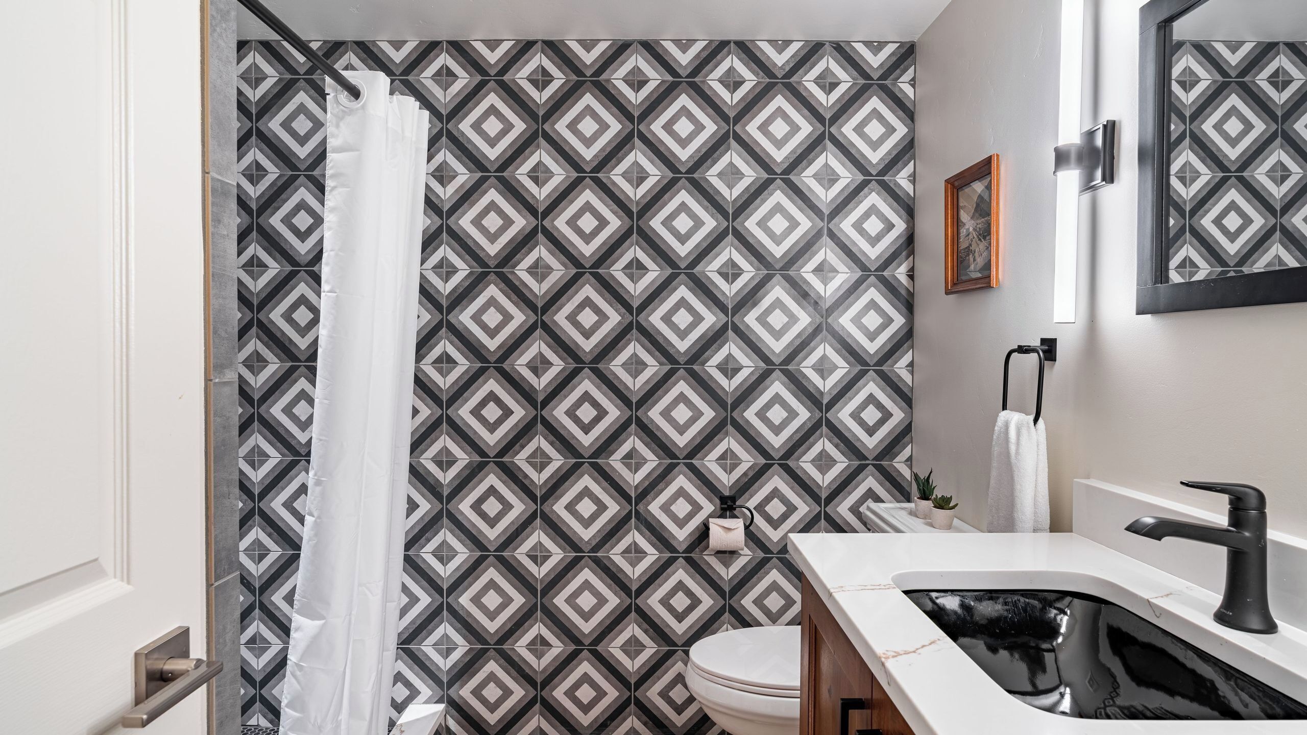Een badkamer met een betegelde muur, een wit toilet, een wastafel met een zwarte kraan en een douchegordijn.