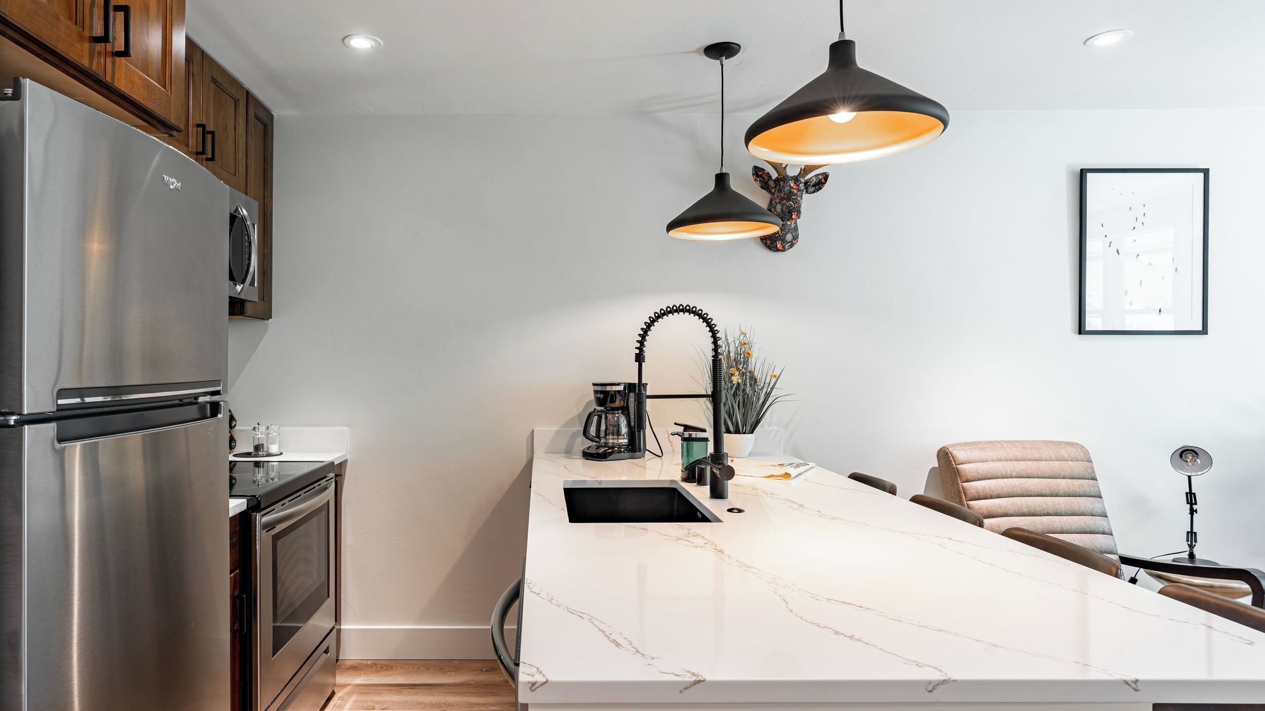 A modern kitchen with a stainless steel refrigerator, a marble countertop, and two pendant lights.