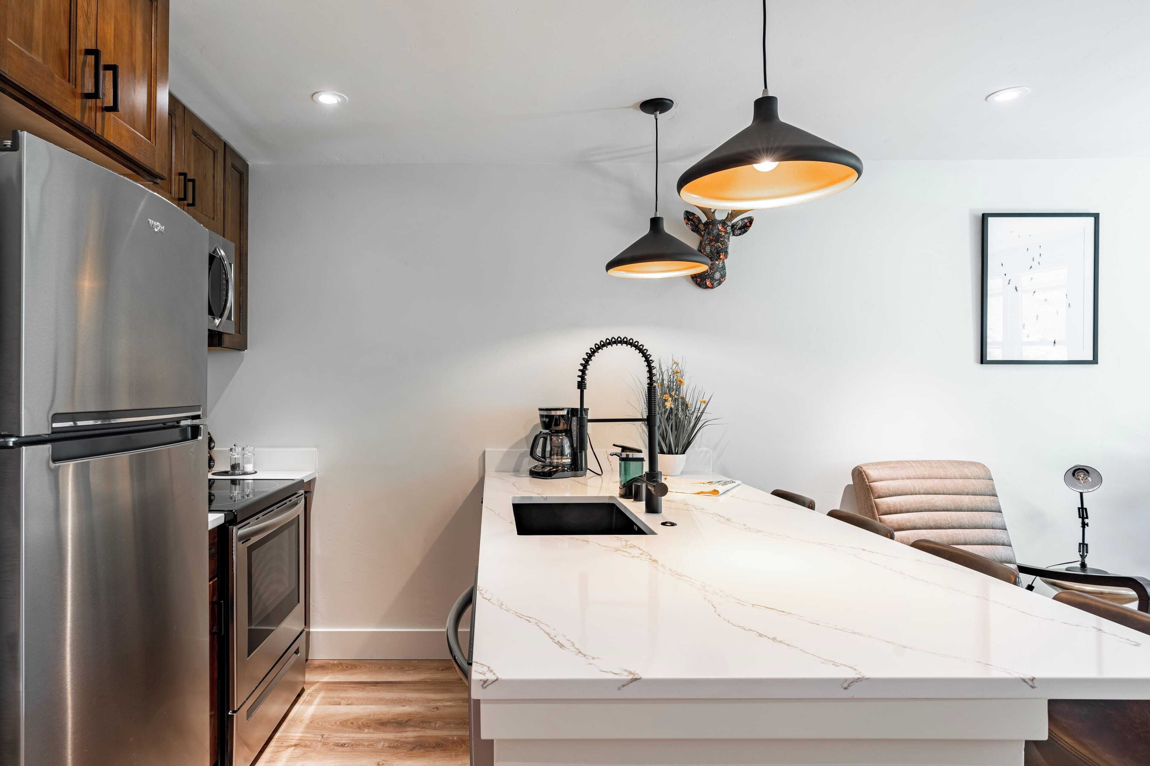 A modern kitchen with a large island, stainless steel appliances, pendant lighting, and a minimalist design.