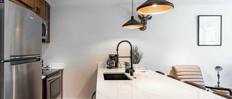 Una cocina moderna con una isla grande, electrodomésticos de acero inoxidable, iluminación colgante y un diseño minimalista.