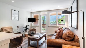 A modern living room with a sofa, coffee table, TV, and a view of a mountain landscape.