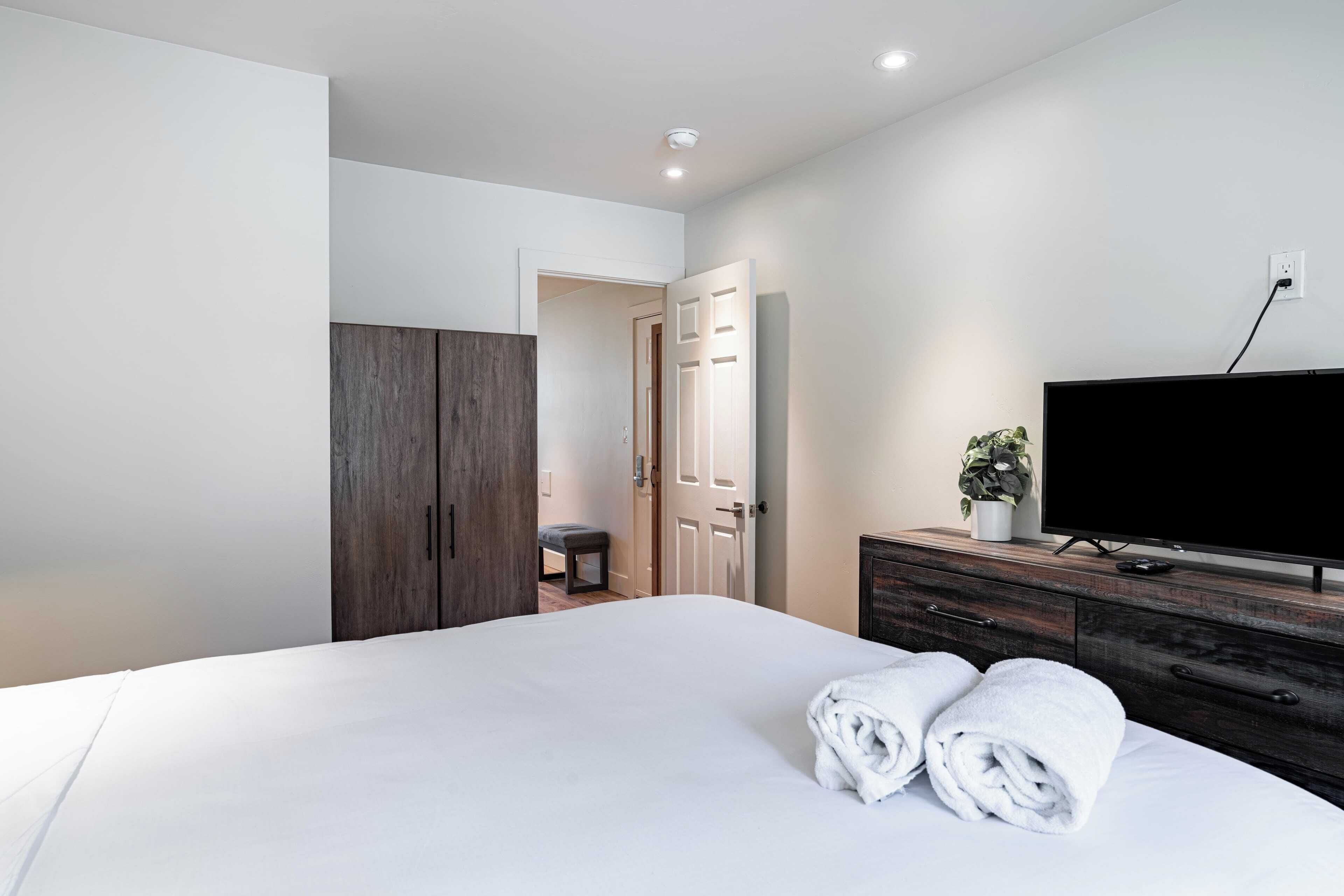 A bedroom with a large bed, a TV, a dresser, and a wardrobe.