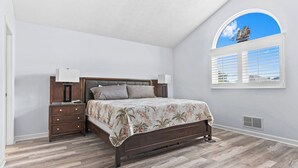 Ein Schlafzimmer mit Bett, Nachttischen, Deckenventilator, Fenster mit Blick und Lüftung.