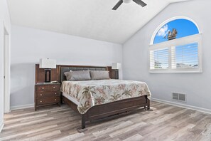 A bedroom with a bed, nightstands, a ceiling fan, a window with a view, and a vent.