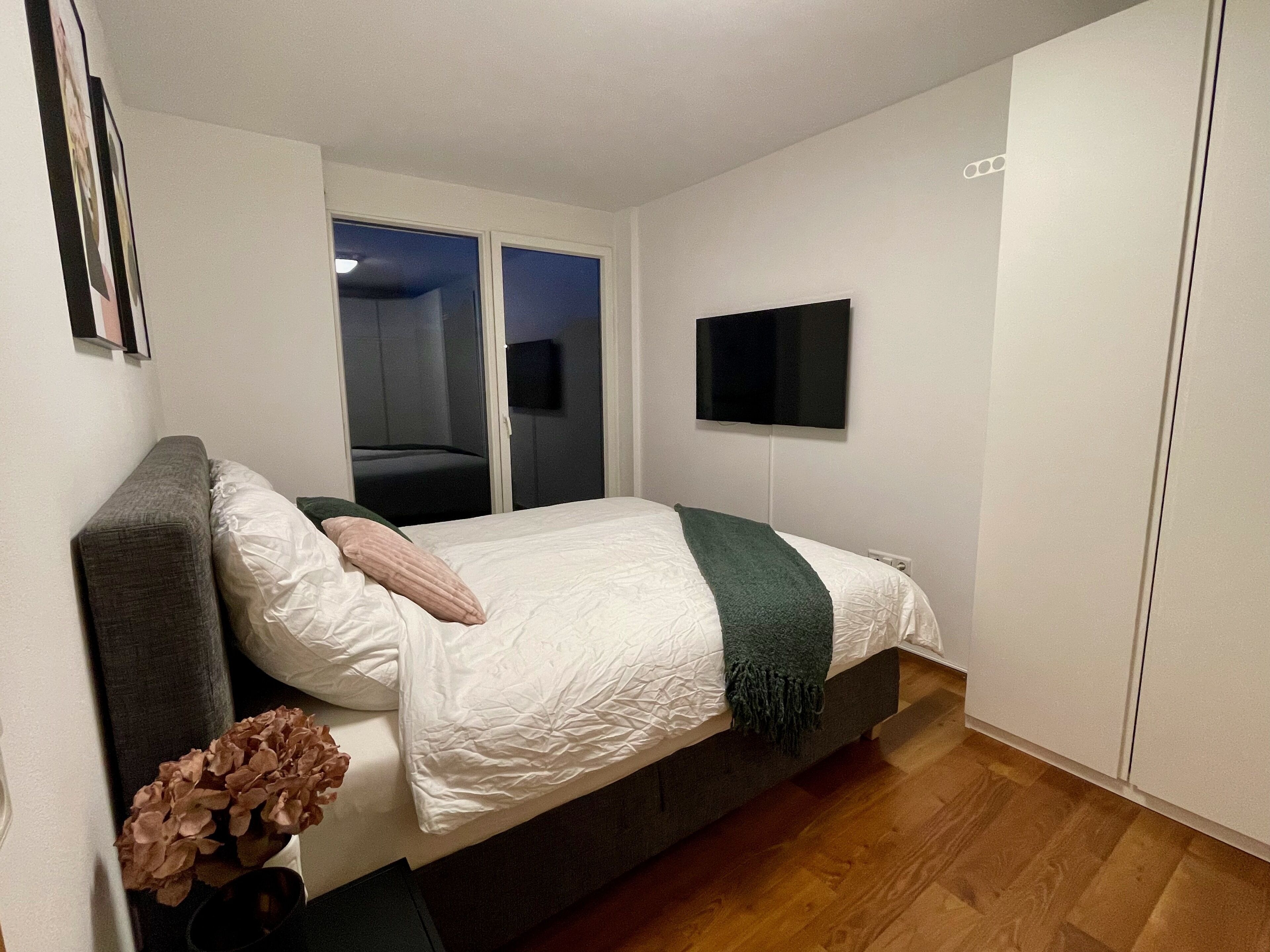 A bedroom with a bed, a TV, a wardrobe, and a window.