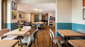 Un espace repas moderne, doté de plusieurs tables et chaises, d’une machine à café et d’œuvres d’art accrochées aux murs.