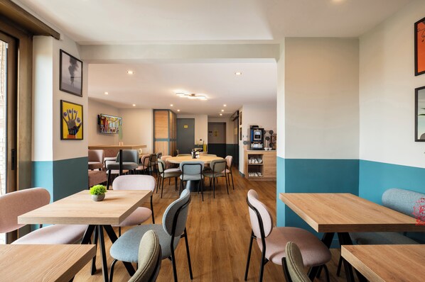 A modern dining area with multiple tables and chairs, a coffee machine, and artwork on the walls. - Rome Ciampino Smart Hotel (Ciampino)