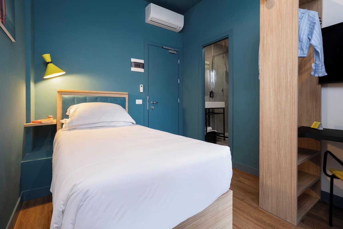 A neatly arranged hotel room with a bed, bedside lamp, and a small table.