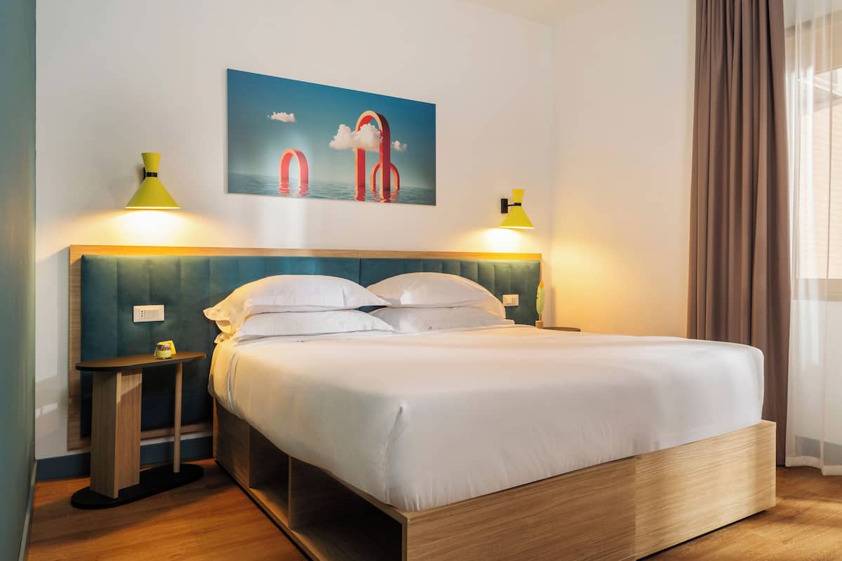 A neatly made bed with a wooden headboard, two bedside tables with lamps, and a painting above the bed.