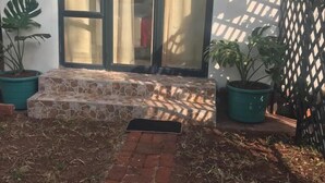 Un espace patio agrémenté d’un banc en pierre, de plantes en pot et d’un chemin en briques menant à une porte-fenêtre coulissante.