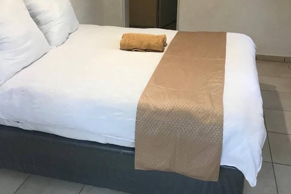 A neatly made bed with white linens and a brown throw blanket, a dark-colored headboard, and a tiled floor.