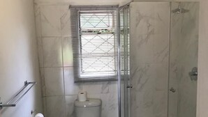Une petite salle de bain avec des toilettes, une douche et une fenêtre.