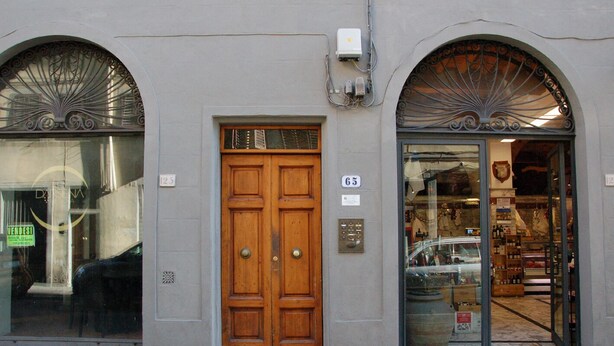 Fachada de edificio con puerta central de madera, dos ventanas arqueadas y entrada a tienda con escaparate de vidrio.