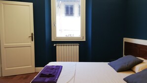 Un dormitorio con cama, dos almohadas, un radiador, una ventana y una puerta.