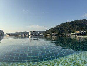 A waterfront hotel with a pool, buildings, and a forested hill in the background. - Zephyr Grand Hotel (Patong)