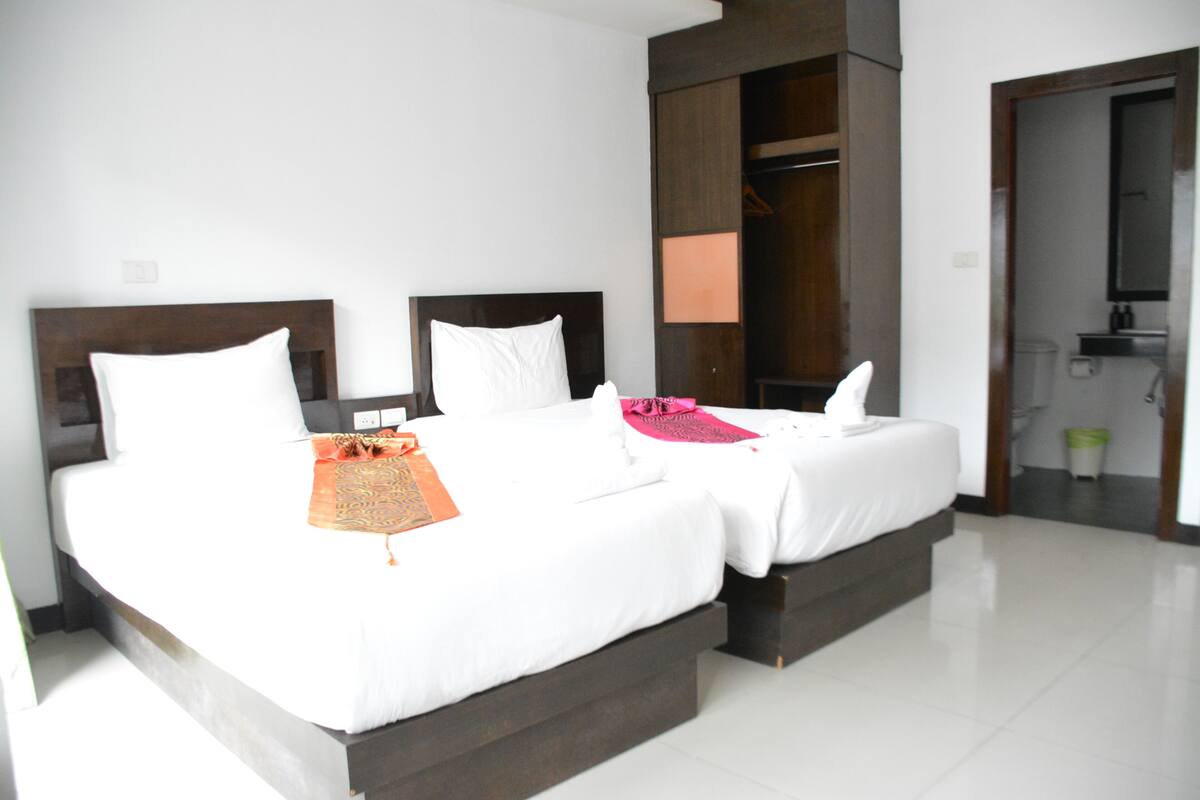 A hotel room with two beds, a wardrobe, and a bathroom visible through an open door.