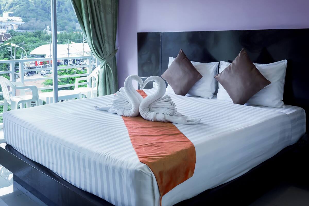 A neatly made bed with a heart-shaped towel arrangement, a peach-colored throw, and three pillows.