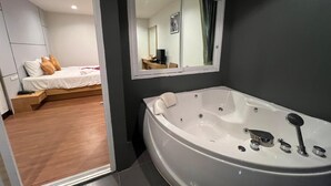 A modern bathroom with a large bathtub, a mirror above it, and a wooden floor. - Zephyr Grand Hotel (Patong)