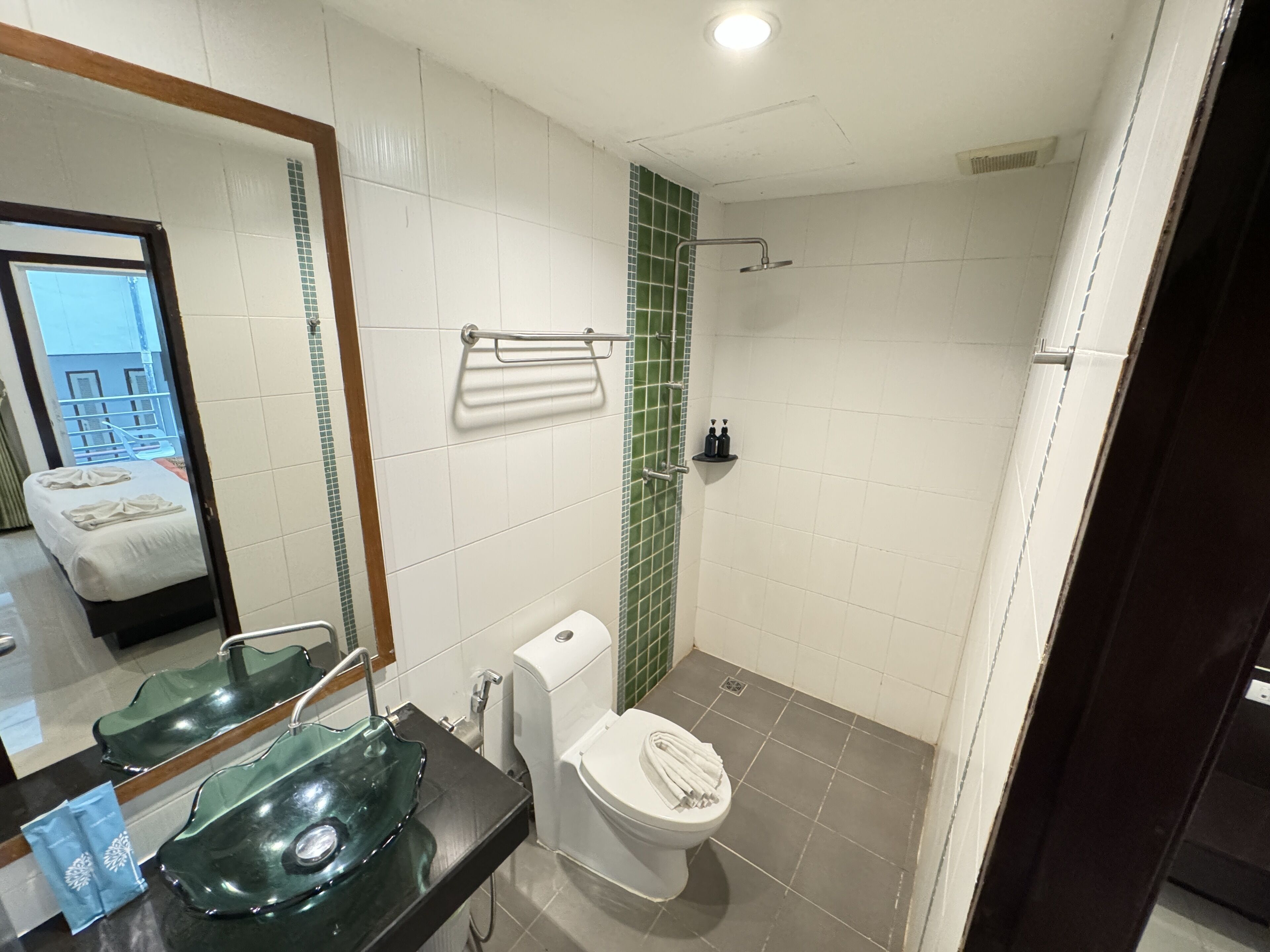 A bathroom with a glass sink, white toilet, and a shower area.
