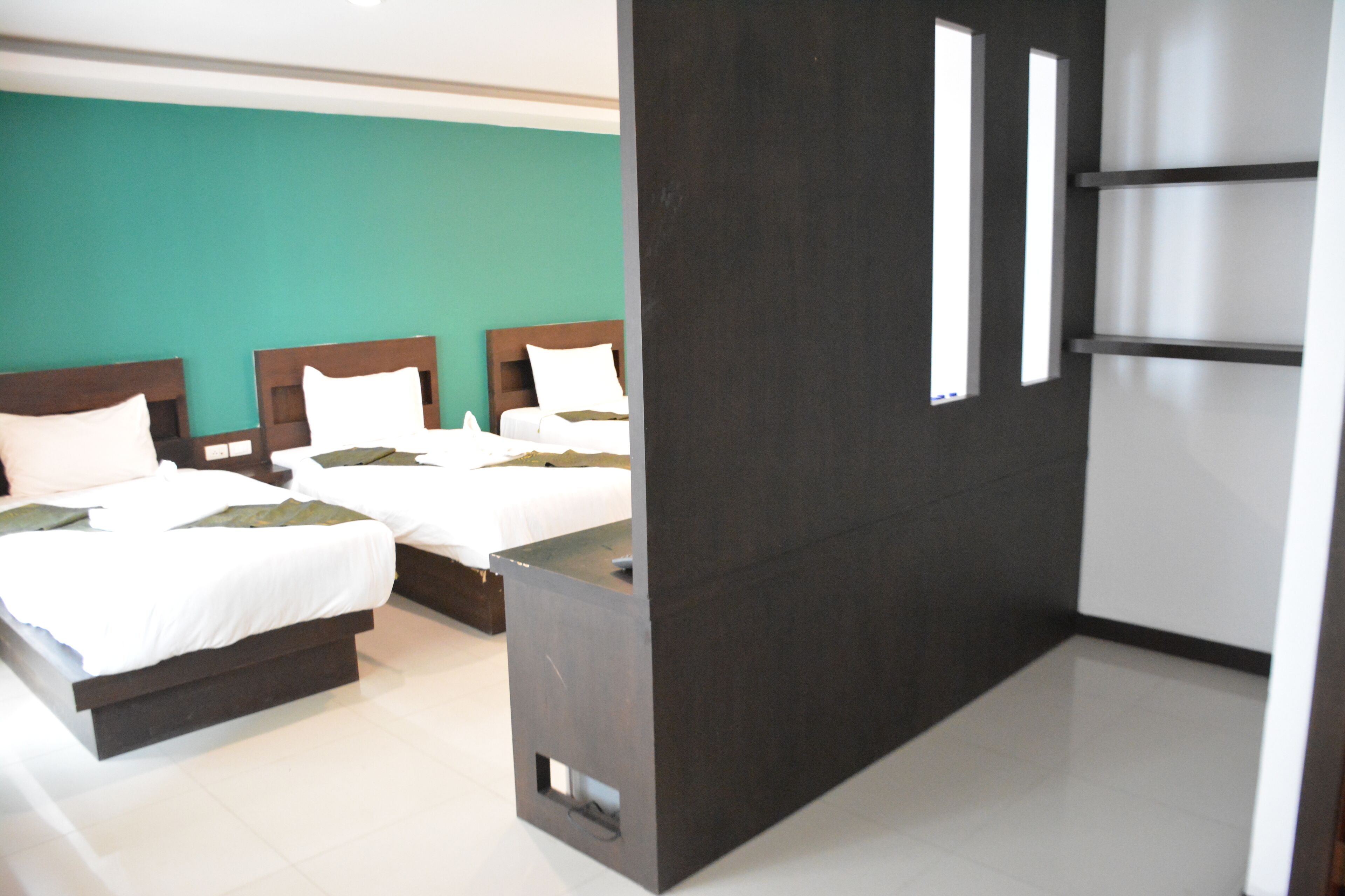A hotel room with three beds, a dark accent wall, and a large window.