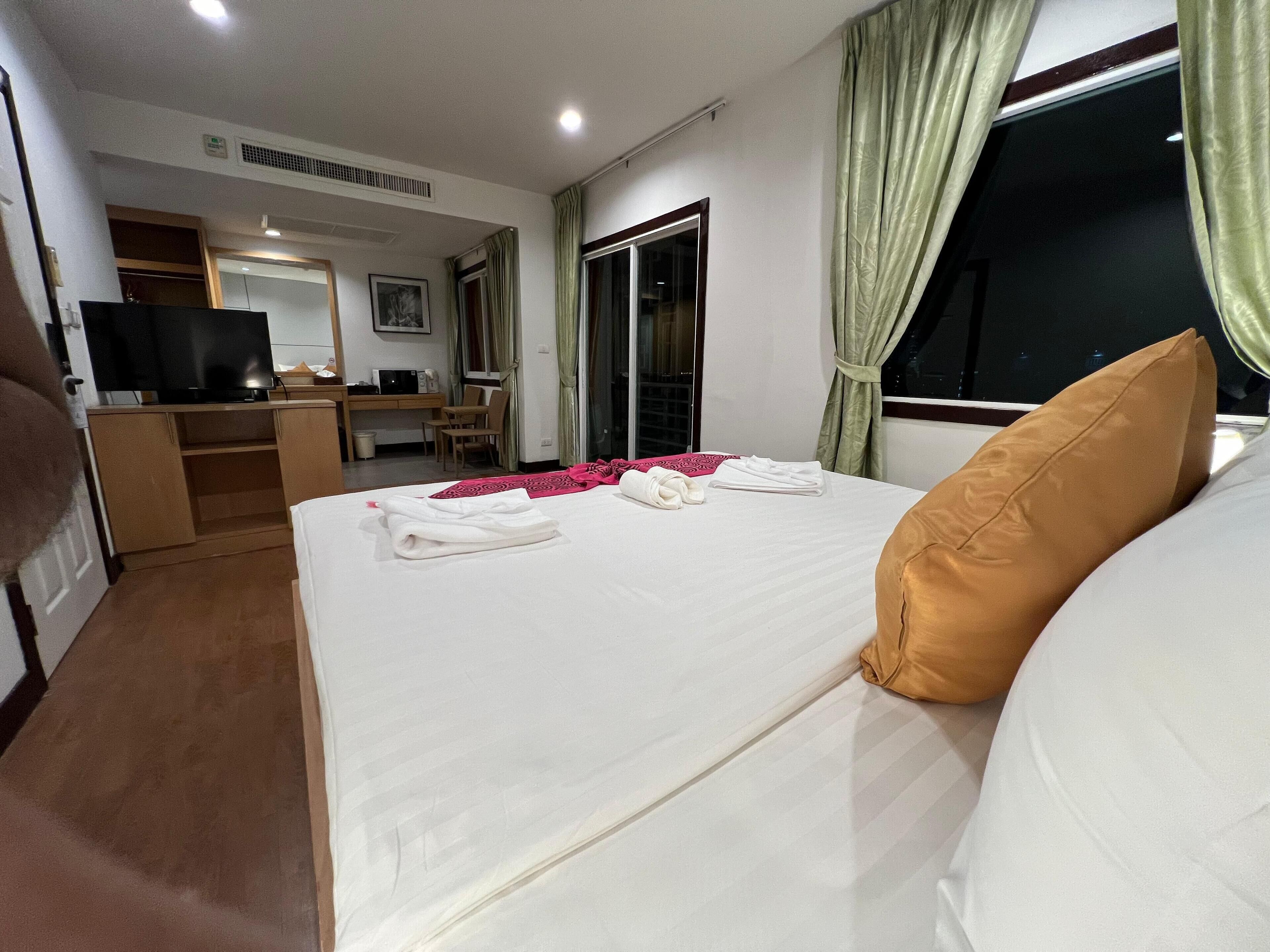Una habitación de hotel con cama, escritorio, televisor y ventana con cortinas.