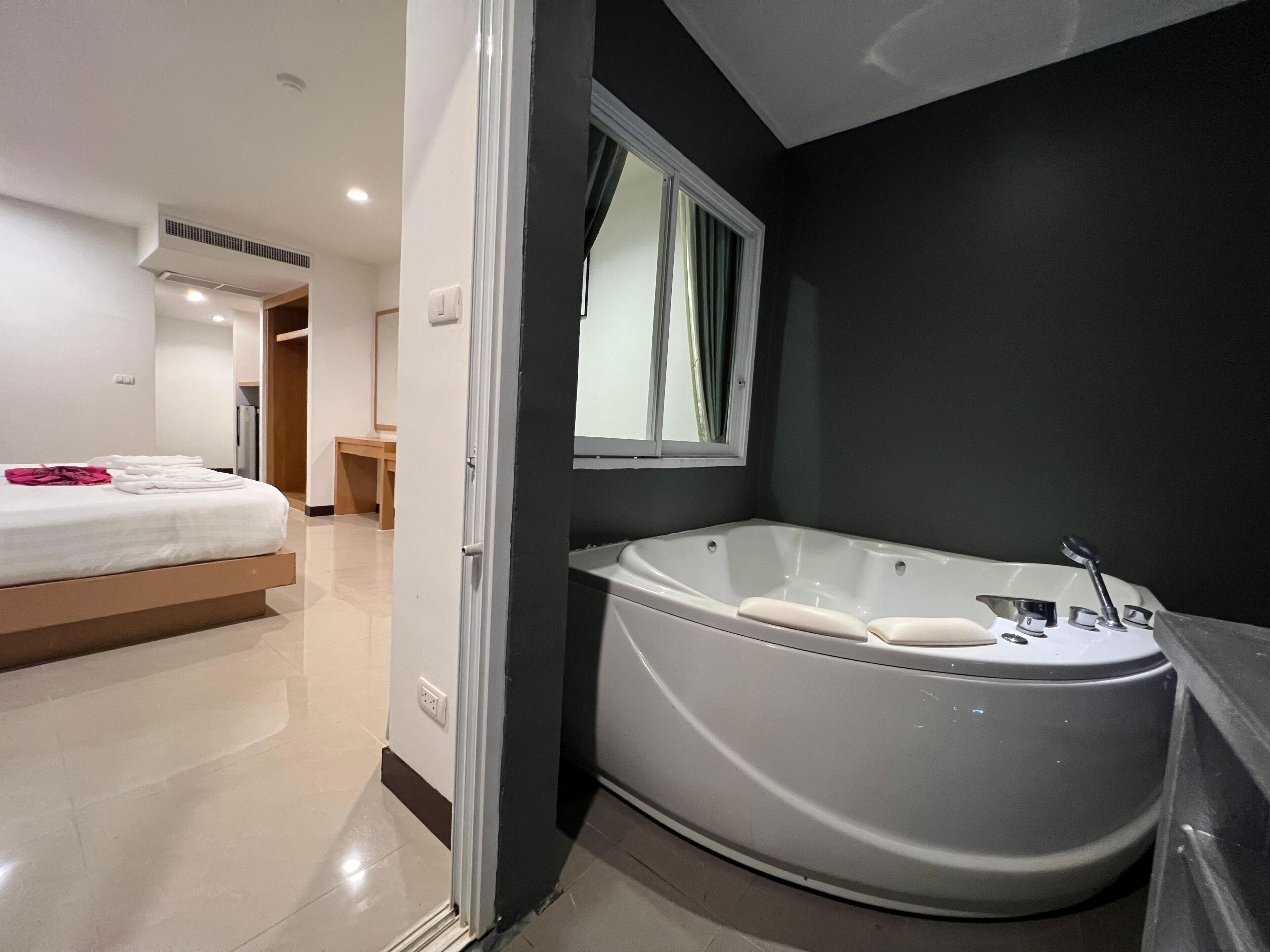 Una habitación de hotel moderna con una bañera grande, un dormitorio independiente con cama y una pequeña zona de estar.