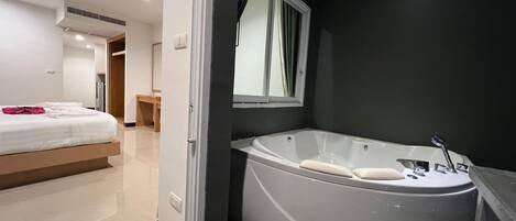 Una habitación de hotel moderna con una bañera grande, un dormitorio independiente con cama y una pequeña zona de estar.
